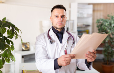Fototapeta premium Portrait of confident young male doctor reading documents at medical office
