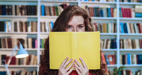Portrait of playful red head pretty girl with long curly natural hair and yellow books having fun...