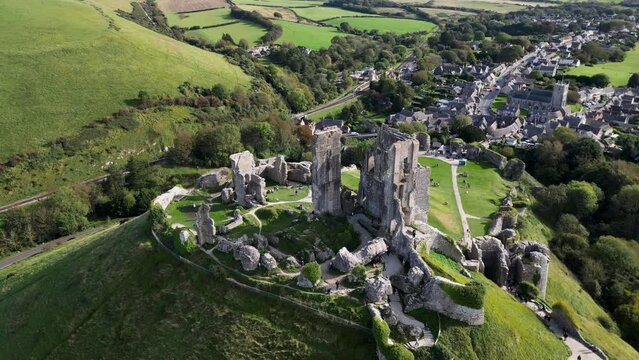 Aerial shot ruins of Corfe Castle on hill with scenery passing in the background on autumn day. Top cinematic aerial view. United Kingdom aerial. 