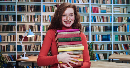 Portrait of cute red head student with long curly natural hair and freckles carrying lots of books...