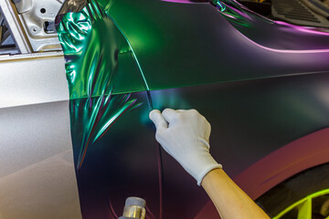 A specialist in wrapping a car with chameleon-colored vinyl film in the process of work. Car...