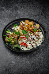 Baked potato slices with stewed vegetables in a cream sauce in a dark plate