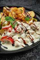 Baked potato slices with stewed vegetables in a cream sauce in a dark plate