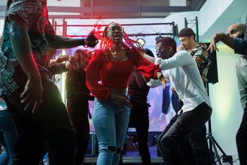 People improvising dance battle while clubbing at nightclub disco party. Young carefree diverse friends making energetic moves on crowded dancefloor at social gathering event