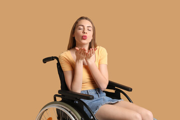 Fototapeta na wymiar Young woman in wheelchair blowing kiss on beige background