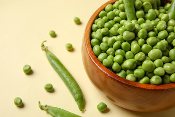 Bowl with fresh green peas on yellow background