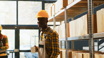 African american warehouse worker posing near shelves filled with products in boxes. Young man with...