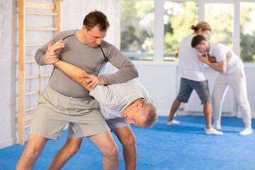 Concentrated men in sport club during self-defense training, sparring and practicing technique of...