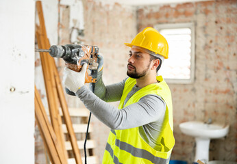 Professional builder working on a construction site during the capital repairs of a house drills a wall with a hammer drill