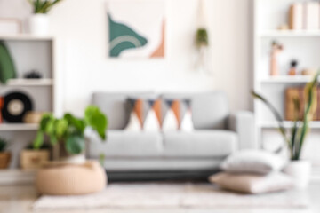 Blurred view of living room with grey sofa, cushions and shelving units