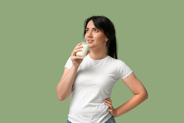 Pretty young woman drinking milk on green background