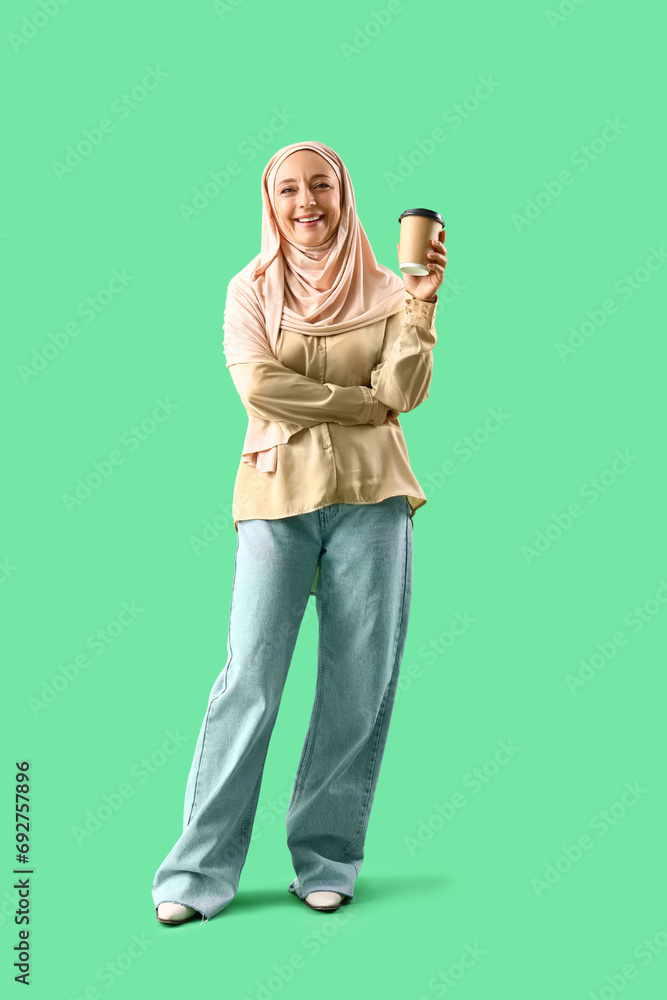 Wall mural Mature Muslim woman with cup of coffee on green background