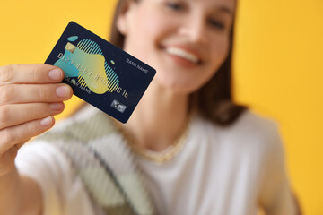 Young woman with credit card on yellow background, closeup