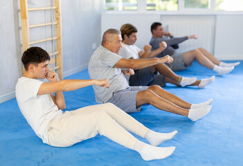 Group of men of different ages train abdominal muscles and do punches at the same time during karate or judo training