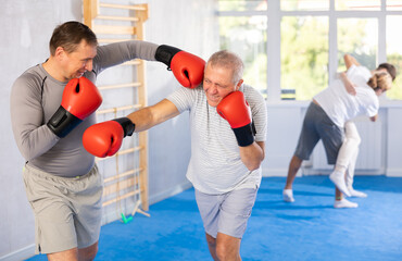 Male co-participant and senior man in boxing gloves strike deliver hook each other, opponent during...