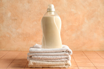 Stack of clean towels with bottle of laundry detergent on beige tiled table