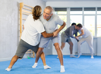 Adult man and elderly men judokas practicing judo technique in gym..