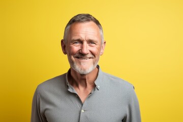 Portrait of a happy senior man smiling at the camera on yellow background