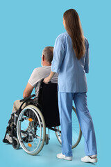 Senior man in wheelchair with nurse on blue background, back view