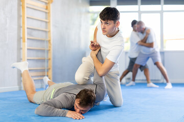 Fototapeta na wymiar Man and young guy in self-defense training practice effective technique of grabbing arm and lowering partner to mat
