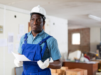 African-american man construction worker holding document in hand while standing in building site,...