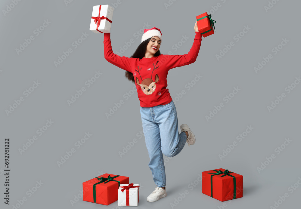 Poster Happy young woman in Christmas sweater with gift boxes on grey background