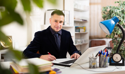Portrait of positive young adult man at workplace in office