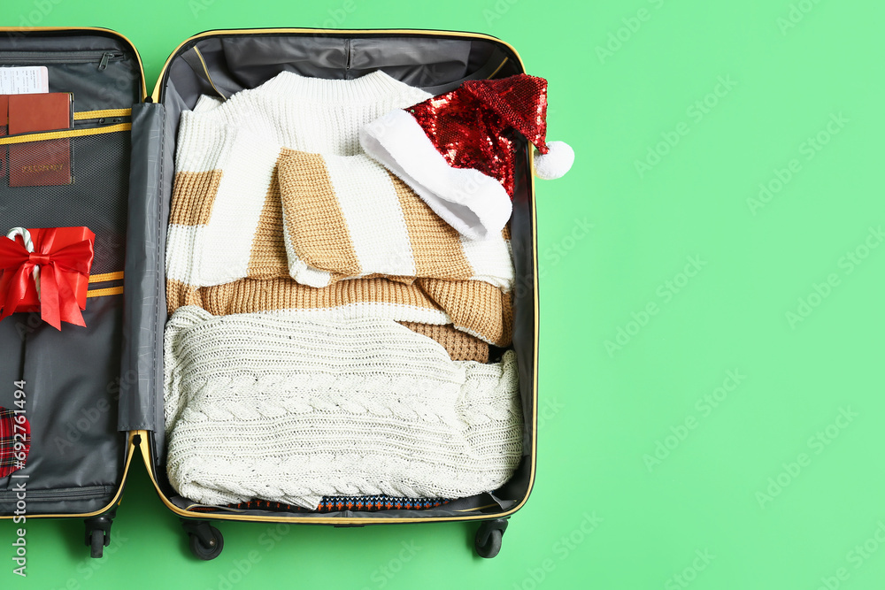 Wall mural Open suitcase with clothes, Christmas gift, passport and Santa hat on green background