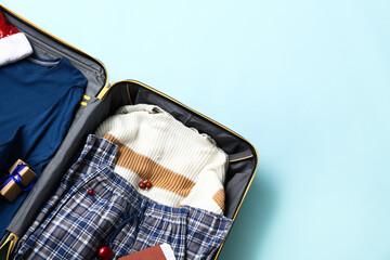 Open suitcase with clothes, Christmas balls and gift on color background