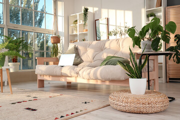 Interior of light living room with green plants and laptop on sofa