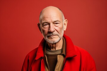 Portrait of an elderly man in a red coat on a red background.