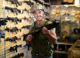 Adult guy in military equipment with weapon in army shop