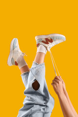 Woman in stylish sneakers tying shoe laces on color background, closeup