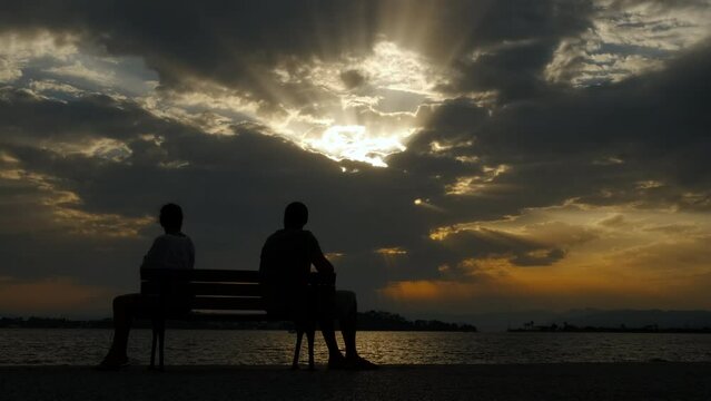 Sad couple on bench on evening beach. A view of stressed couple sitting on bench after a quarrel on the beach during evening time.