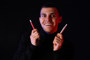 Young man with electronic cigarettes on black background