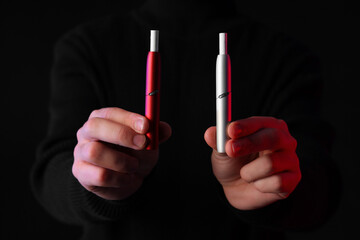Young man with electronic cigarettes on black background, closeup