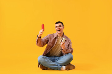 Young man with electronic cigarettes on yellow background