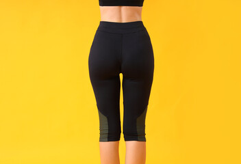 Young woman in black cycling shorts on yellow background, back view