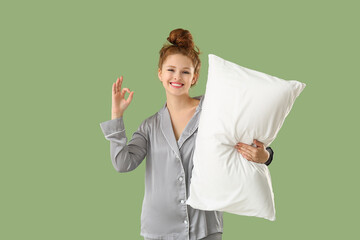 Beautiful young woman holding white soft pillow and showing ok gesture on green background