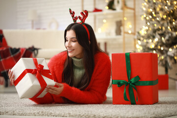 Beautiful young woman in reindeer horns with gifts at home on Christmas eve