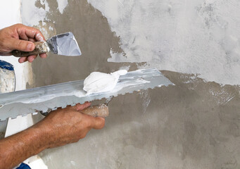 Worker puts finishing layer of stucco on the wall using a plastering trowel - 692770458