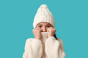 Cute little girl wearing warm hat and sweater on blue background