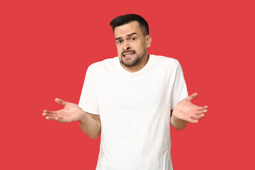 Handsome ashamed young man shrugging on red background
