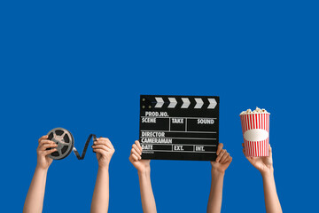 Female hands with movie clapper, reel and bucket of popcorn on blue background - obrazy, fototapety, plakaty