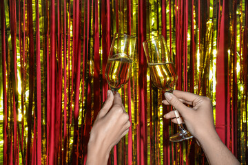 Female hands with glasses of champagne and golden tinsel on red background