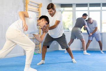 Obraz premium Adult man and young guy training judo techniques in studio..