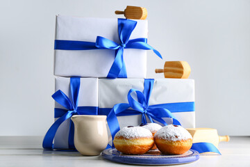 Gifts for Hanukkah celebration, tasty donuts and and dreidels on light background