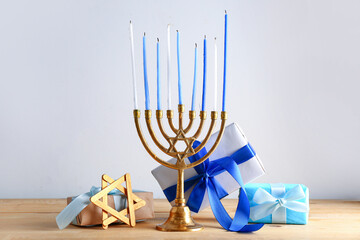 Menorah, David star and gifts for Hanukkah celebration on wooden table against light background