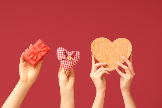 Female hands with gift box, wooden and fabric hearts on red background. Valentine's Day celebration