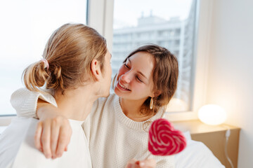 Young man and woman hugging sitting at home looking at each other beautiful female holding red heart